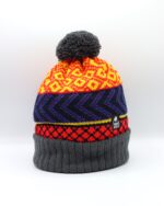 The Ultra Wonky hat is knitted with a grey pompom and turn up. Sandwiched between is the triple pattern area knitted in vibrant red and yellow with navy and purple contrasting features.