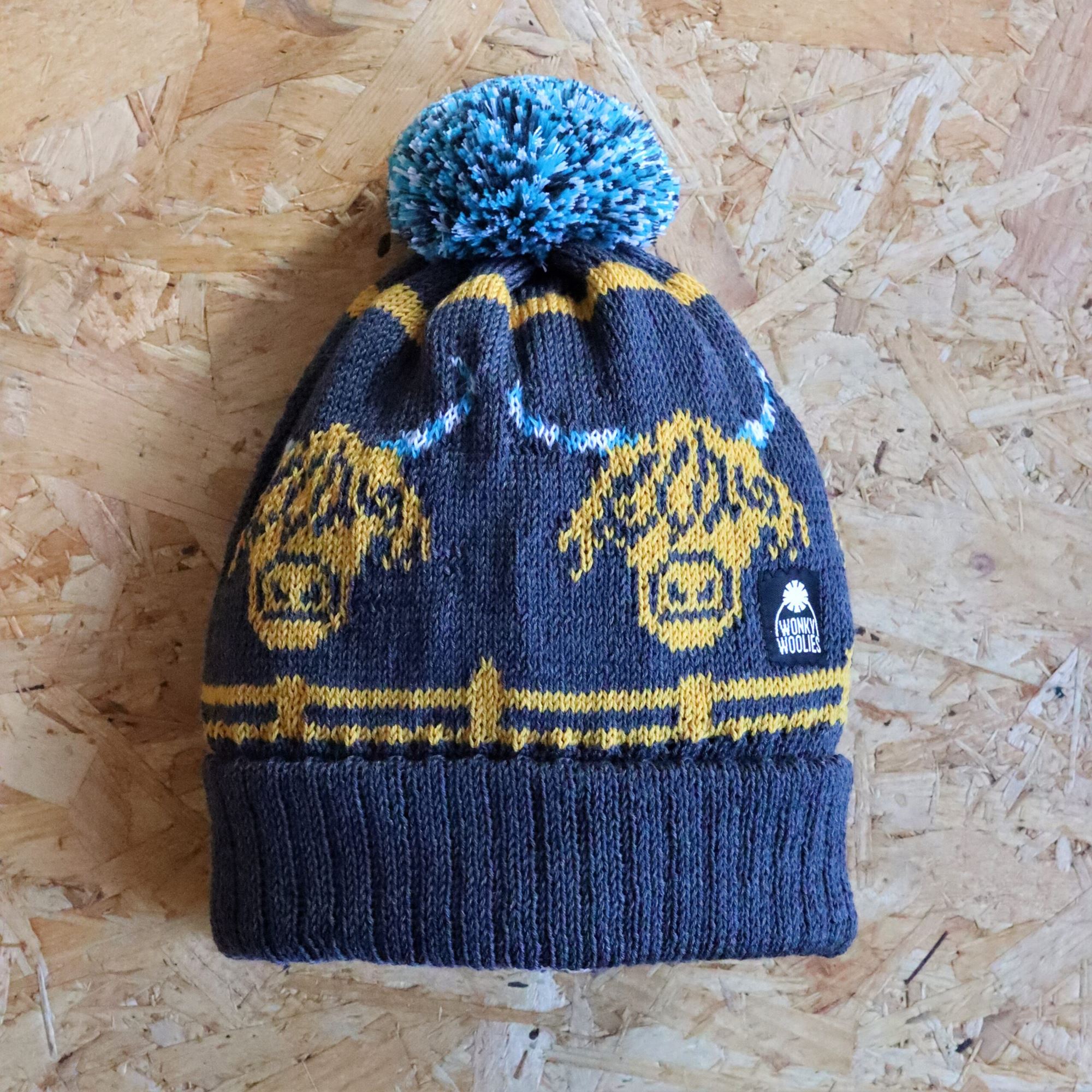 A bobble hat with a large highland cow face repeated 4 times. The cow has candy cane horns in contrasting colours.