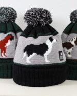Image of three pompom hats with dogs knitted into them, a boxer dog, a border collie and a springer spaniel.