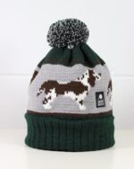 A product photo of a bottle green pompom hat with a Springer spaniel dog design knitted into it.