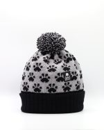 Product shot of a black and silver coloured pompom hat with black paw prints all over it.