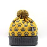 Product shot of a pompom hat with a paw print pattern knitted into it. The hat turn up is charcoal grey with the main hat being mustard with grey paw prints.