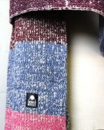 Close image of a blanket scarf with block colours of pink, blue and burgundy on a cream background.