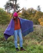Image of a woman wearing a purple blanket scarf fanned out like a cape.